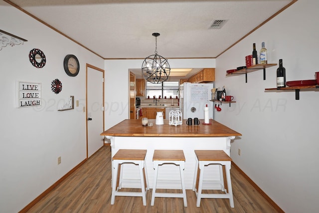 kitchen featuring freestanding refrigerator, light wood-style floors, ornamental molding, a chandelier, and a sink