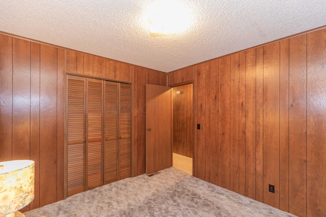 unfurnished bedroom with wood walls, carpet floors, a textured ceiling, and a closet