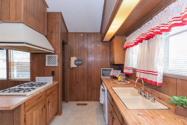 kitchen featuring a textured ceiling, wood walls, white gas cooktop, and sink