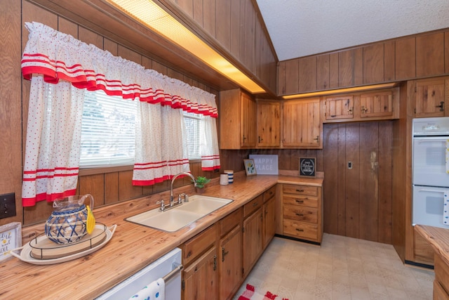 kitchen featuring a textured ceiling, white appliances, sink, lofted ceiling, and wood walls