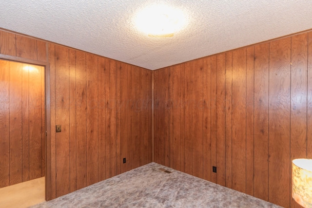 empty room featuring wood walls, carpet floors, and a textured ceiling