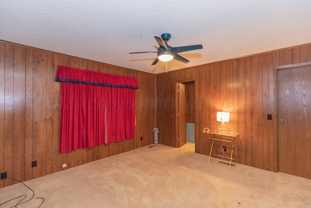 unfurnished room featuring carpet, ceiling fan, a textured ceiling, and wooden walls