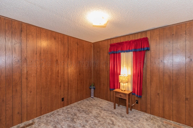 carpeted empty room featuring a textured ceiling and wooden walls