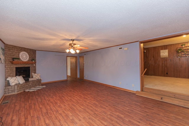 unfurnished living room featuring ceiling fan, a brick fireplace, a textured ceiling, wooden walls, and hardwood / wood-style flooring