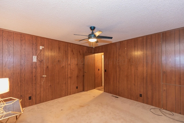 empty room with carpet flooring, ceiling fan, a textured ceiling, and wooden walls