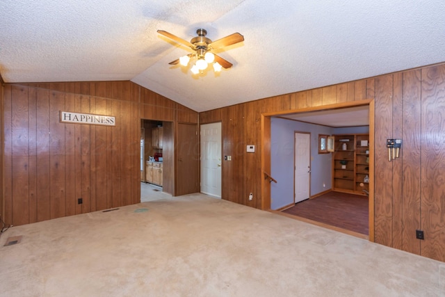 unfurnished room featuring light colored carpet, vaulted ceiling, ceiling fan, and wood walls