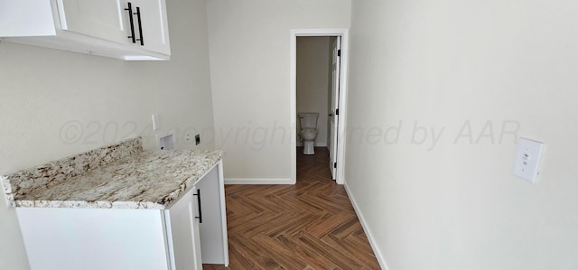 kitchen featuring white cabinets, light stone countertops, and dark parquet flooring