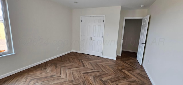 unfurnished bedroom featuring dark parquet flooring and a closet