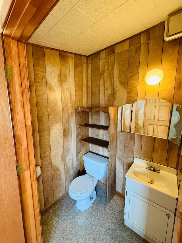 half bathroom featuring vanity, toilet, and wood walls