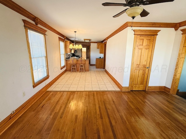 unfurnished dining area featuring ceiling fan with notable chandelier, light wood-style floors, baseboards, and ornamental molding