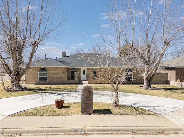 ranch-style home with curved driveway, a front yard, a shingled roof, brick siding, and a chimney