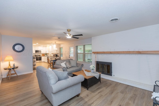 3301 Palmetto Trl, Amarillo, TX 79106 - living area with light wood-type flooring, a ceiling fan, baseboards, a brick fireplace, and a textured ceiling