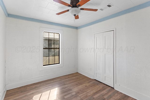 unfurnished bedroom with ceiling fan, wood-type flooring, a closet, and multiple windows