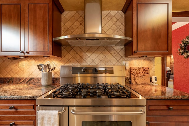 kitchen with gas range, wall chimney range hood, tasteful backsplash, dark stone counters, and brown cabinetry