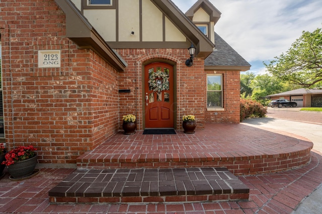 doorway to property featuring brick siding, stucco siding, and roof with shingles