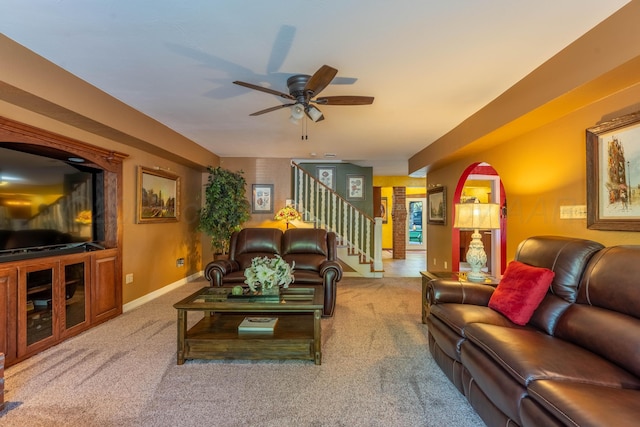 living area with carpet floors, a ceiling fan, stairs, and baseboards