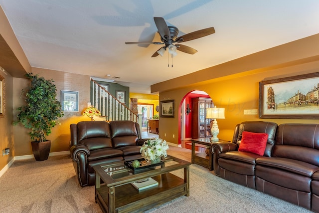 carpeted living area featuring arched walkways, baseboards, a ceiling fan, and stairs