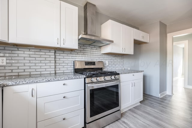 kitchen featuring stainless steel gas stove, white cabinetry, light stone counters, decorative backsplash, and wall chimney exhaust hood