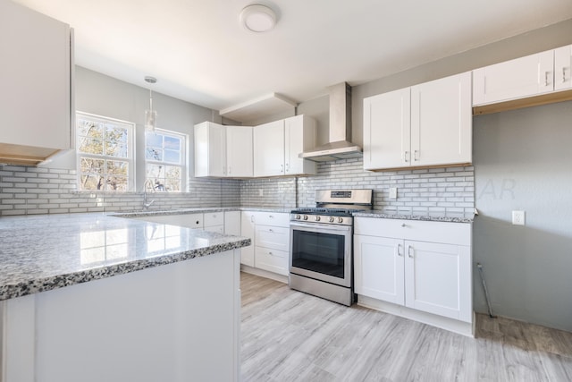 kitchen with gas range, wall chimney range hood, decorative light fixtures, and white cabinets