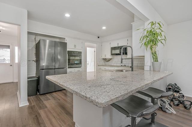 kitchen with sink, light stone counters, black appliances, white cabinets, and kitchen peninsula