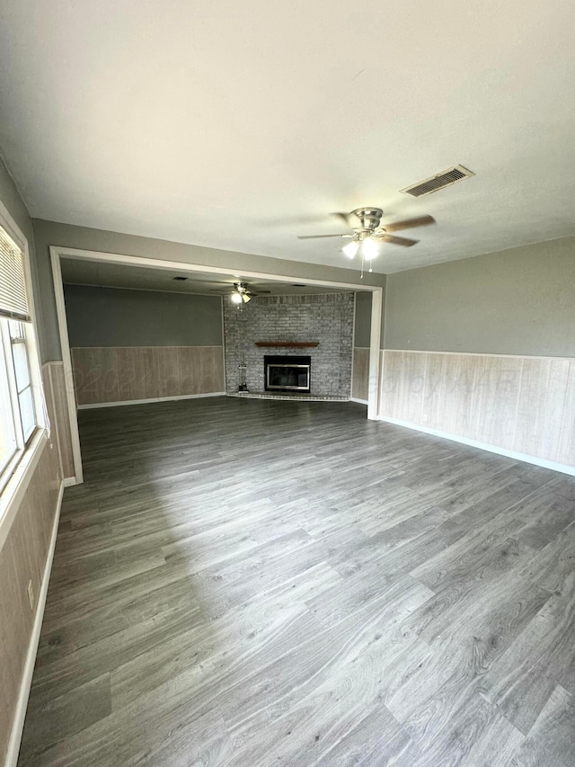 unfurnished living room with ceiling fan, a fireplace, wooden walls, and hardwood / wood-style flooring