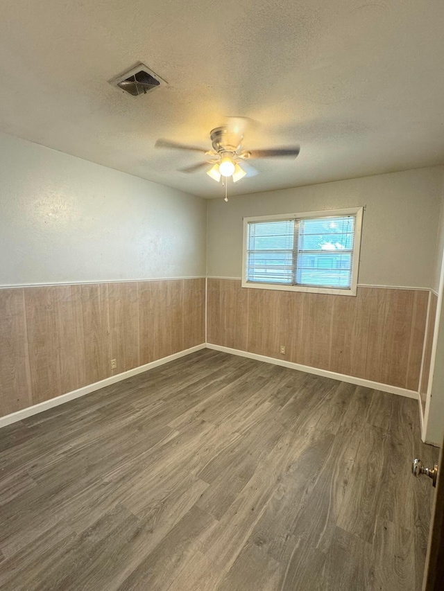 spare room featuring dark hardwood / wood-style floors, ceiling fan, a textured ceiling, and wooden walls