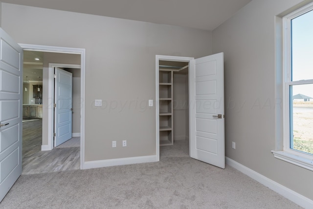 unfurnished bedroom with carpet flooring, a walk in closet, and baseboards