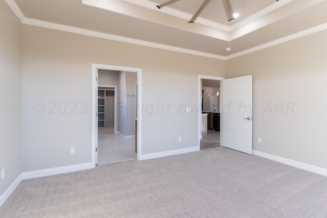 unfurnished bedroom featuring ornamental molding, a walk in closet, light carpet, and baseboards