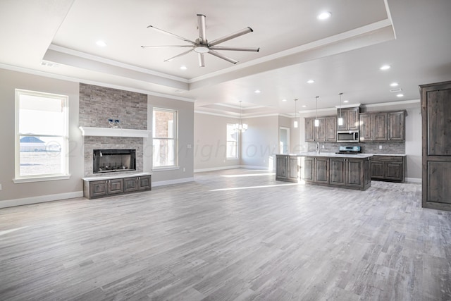 unfurnished living room featuring light wood-style floors, baseboards, a tray ceiling, and crown molding