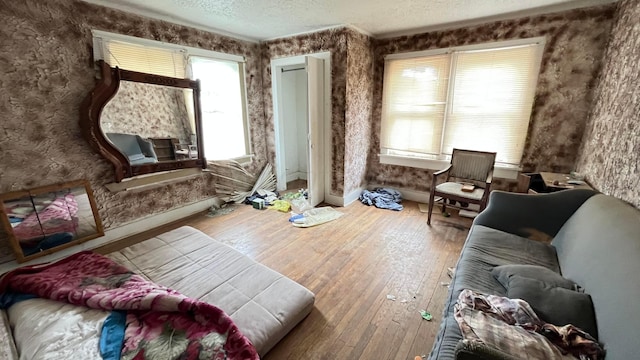 living area featuring wood-type flooring, wallpapered walls, and a textured ceiling