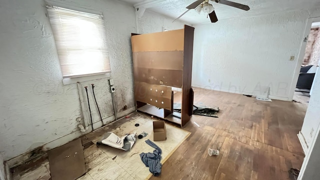 interior space with wood-type flooring, a ceiling fan, and a textured wall