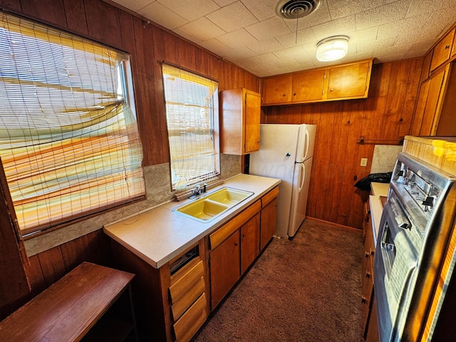 kitchen featuring visible vents, brown cabinetry, freestanding refrigerator, a sink, and wooden walls