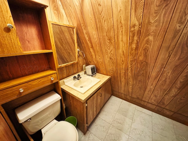 half bathroom featuring marble finish floor, wood walls, vanity, and toilet