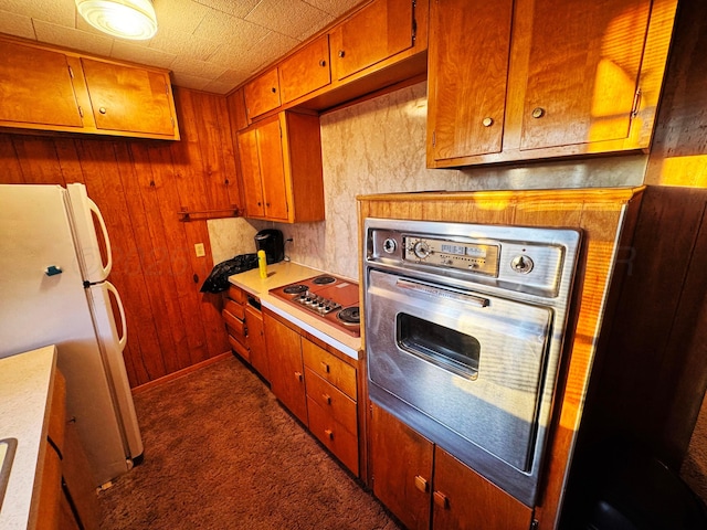 kitchen featuring wooden walls, baseboards, appliances with stainless steel finishes, brown cabinets, and light countertops