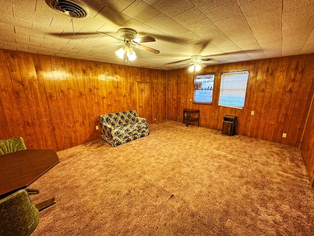 unfurnished room with carpet, wooden walls, visible vents, and ceiling fan