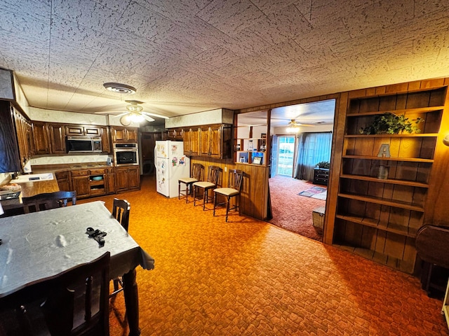 dining room with wooden walls, visible vents, ceiling fan, carpet, and a textured ceiling