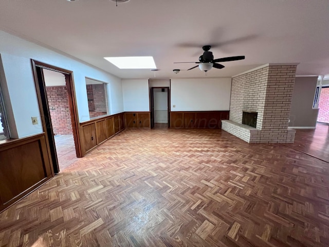 6201 Adirondack Trl, Amarillo, TX 79106 - unfurnished living room featuring wainscoting, a skylight, ceiling fan, a fireplace, and wood walls