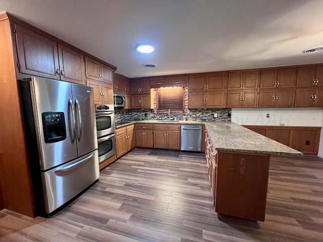 6201 Adirondack Trl, Amarillo, TX 79106 - kitchen featuring stainless steel appliances, a peninsula, wood finished floors, backsplash, and light stone countertops