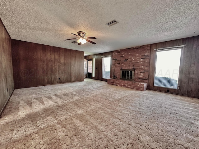 unfurnished living room with ceiling fan, wood walls, visible vents, a brick fireplace, and carpet