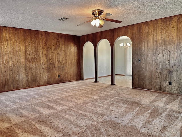 empty room with arched walkways, a textured ceiling, wooden walls, light colored carpet, and visible vents