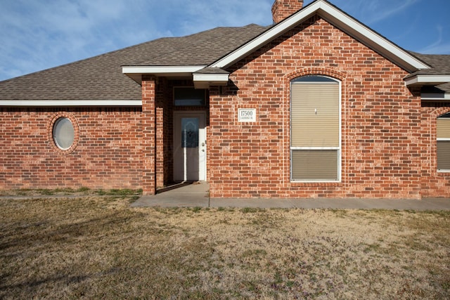 exterior space featuring a lawn, a chimney, brick siding, and a shingled roof