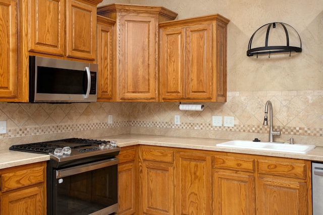 kitchen featuring brown cabinets, a sink, tasteful backsplash, appliances with stainless steel finishes, and light countertops