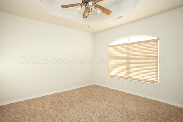 carpeted empty room with visible vents, a raised ceiling, baseboards, and a ceiling fan