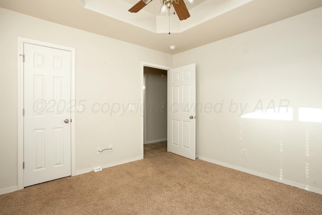 unfurnished bedroom with ceiling fan, a raised ceiling, baseboards, and light carpet