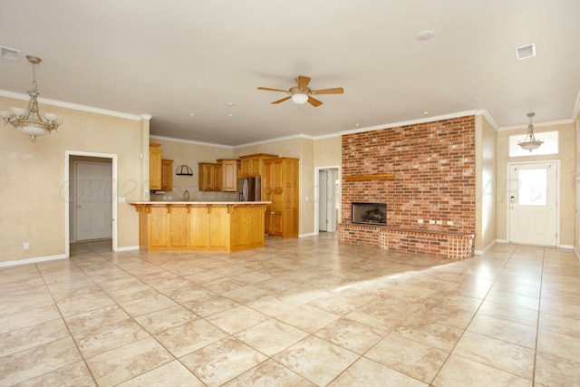 unfurnished living room with ceiling fan with notable chandelier, a fireplace, baseboards, and ornamental molding