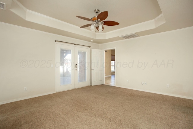 carpeted empty room featuring a raised ceiling, french doors, visible vents, and ornamental molding