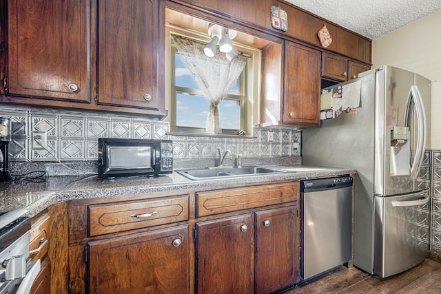 kitchen with a textured ceiling, stainless steel appliances, a sink, decorative backsplash, and dark wood finished floors