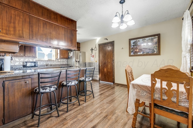 kitchen with a breakfast bar, tasteful backsplash, light wood-style floors, a textured ceiling, and stainless steel fridge