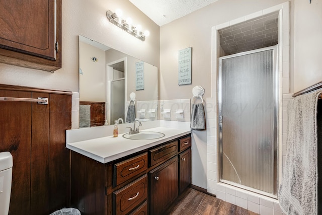 full bathroom featuring wood finished floors, wainscoting, a shower stall, and vanity