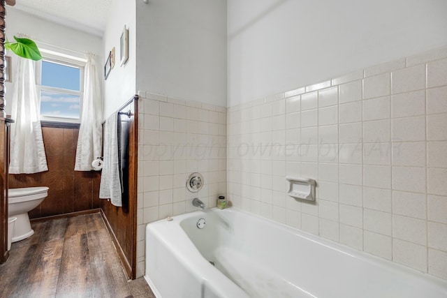 full bathroom with toilet, a bath, and wood finished floors